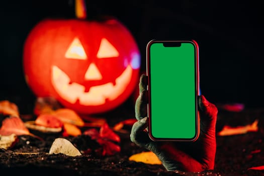 Zombie hand with smartphone. Undead, halloween pumpkin, mobile operator advertising. Terrifying scene from underground. Copy space. High quality