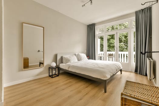 a bedroom with a bed, chair and mirror on the wall in front of the window looking out onto the balcony