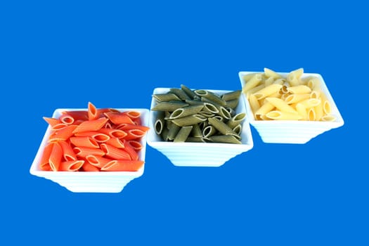 Three white bowls ful of colorful pasta isolated on blue