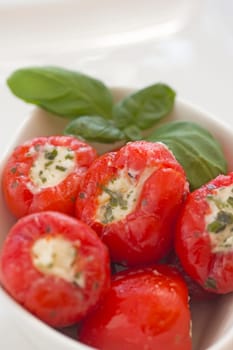 Spicy round red peppers stuffed with cheese, garnished with basil. The white bowl.