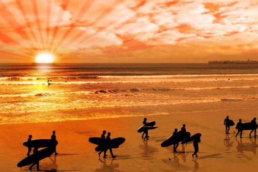 surfers walking on the beach in lahinch county clare ireland as the sun goes down