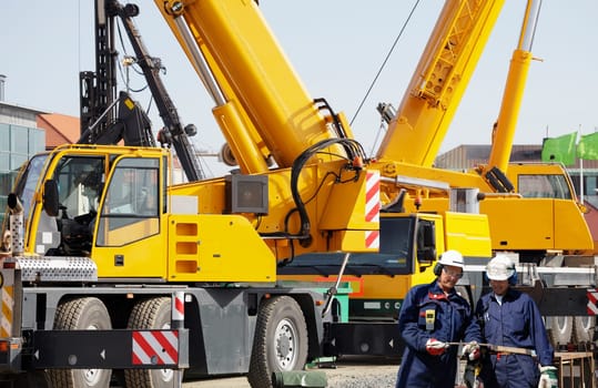 giant mobile cranes, two site workers in the foreground
