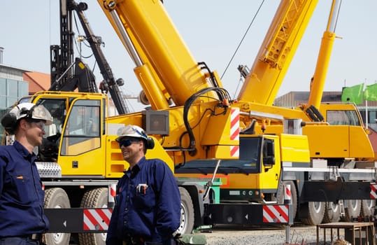 two construction-workers with giant mobile building cranes in background