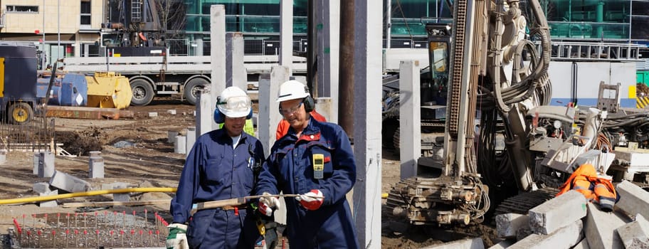 two building engineers with heavy construction machines in background, panoramic view