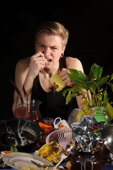 A young man with a cup sits behind dirty table