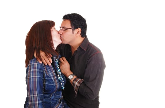 A middle aged couple standing in the studio and kissing each other. She with red hair, blouse sheckered shirt and necklace, over white.