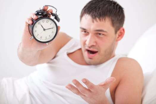 angry man in bed holding alarm clock in his hand