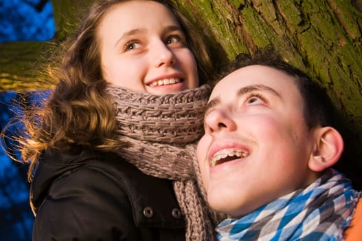 Head and shoulders portraits of two young teenage siblings (brother and sister) laughing at dusk standing by a tree