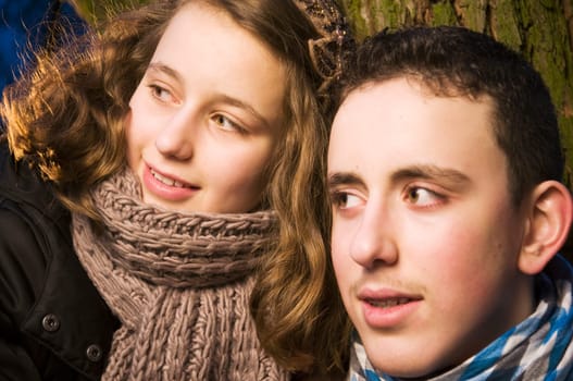 Head and shoulders portraits of two young teenage siblings (brother and sister) laughing at dusk standing by a tree