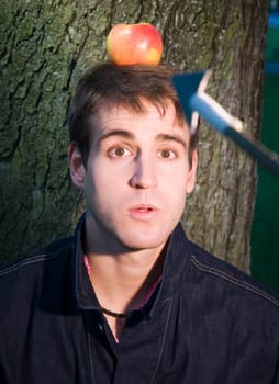 Head and shoulders shot of a young man at the tree with apple on his head and arrow at him from the camera