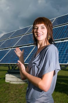 Upper body shot of a young, brunette woman in front of a photovoltaic system in a casual leisure dress on a green meadow in summer.