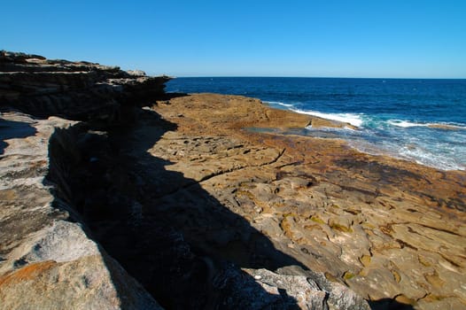 rocky coastline, man lying in distance, clear blue sky