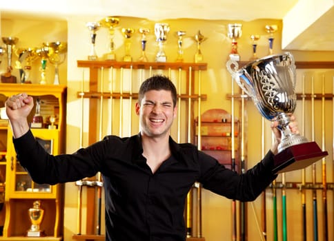 Happy proud winner man with big trophy silver cup in billiard club