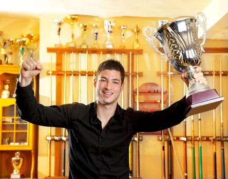 Happy proud winner man with big trophy silver cup in billiard club