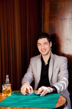 Latin handsome gambler man in table playing poker cards and drinking whisky