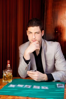 Latin handsome gambler man in table playing poker cards and drinking whisky