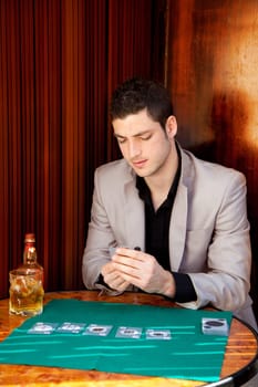 Latin handsome gambler man in table playing poker cards and drinking whisky
