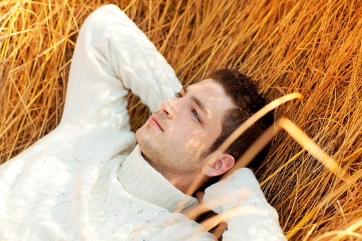 Autumn winter man portrait lying in golden grass field with turtleneck sweater
