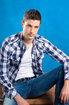 handsome young man with plaid shirt sitting on wood in blue background