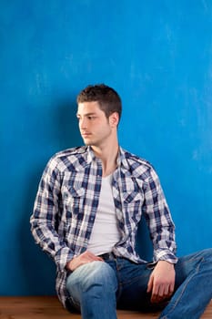 handsome young man with plaid shirt sitting on wood in blue background