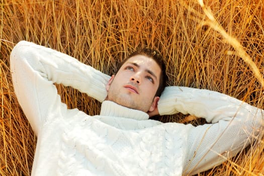 Autumn winter man portrait lying in golden grass field with turtleneck sweater
