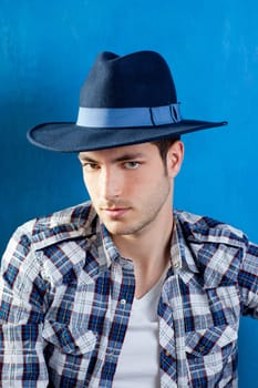 handsome young man with plaid shirt and cowboy hat on blue background
