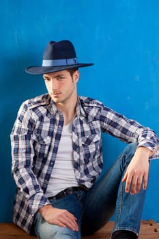 handsome young man with plaid shirt and cowboy hat on blue background