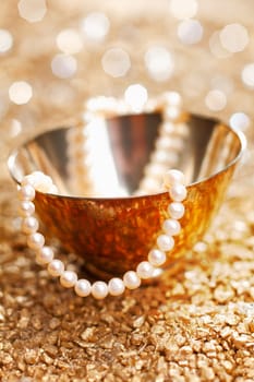 A matched string of pearls cascades down from a pretty silver bowl backed by a bokeh of festive party lights
