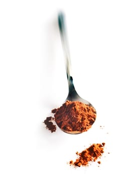 Metal spoon pointing towards the camera filled with chocolate powder which is spilling onto the surface below