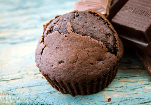 Freshly baked chocolate muffin and pieces of chocolate on rustic wooden blue painted boards