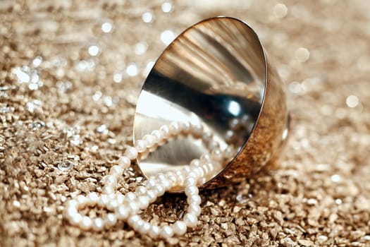 A string of matched pearls spills out of a silver bowl lying on its side with shallow depth of field