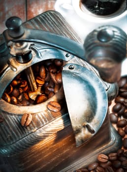 Retro wooden coffee grinder with its top open filled with coffee beans which have spilled out onto the table below