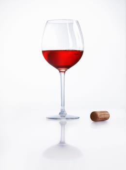 Glass half filled with red wine on a reflective white surface with a cork alongside at a party or celebration