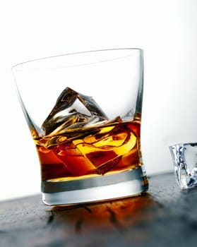 Angled image of a glass of golden whiskey or brandy on the rocks with large ice cubes served on a bar countertop