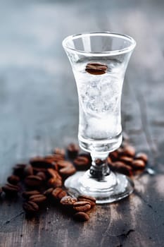 Tall glass with clear sambuca and coffee beans spilled around the base of the glass