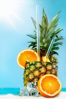 Pineapple with oranges and tubules on white beach sand. Fresh cold drink