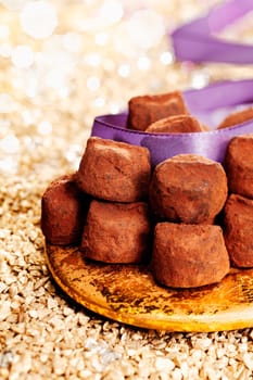 Plate of luxury handmade chocolate confectionery with a purple ribbon and background bokeh of twinkling party lights