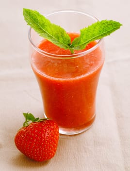 High angle view of a glass of healthy fresh strawberry smoothie and a ripe red strawberry served ready for a vegetarian breakfast
