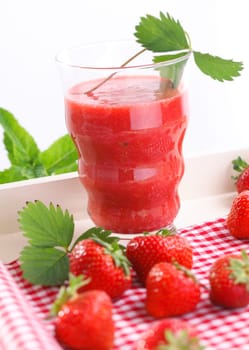 Refreshing strawberry smoothie surrounded by ripe red strawberries on a red and white checked napkin