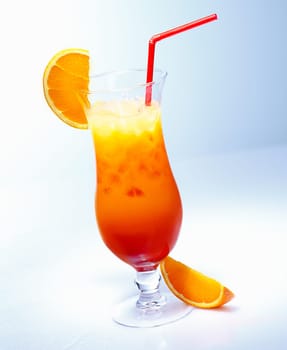 Tall glass of iced fresh fruit orange cocktail with a straw against a pale blue background in a tropical vacation concept