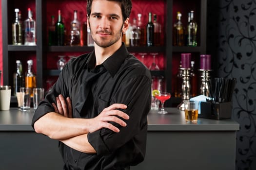Portrait of handsome barman standing in front of the bar