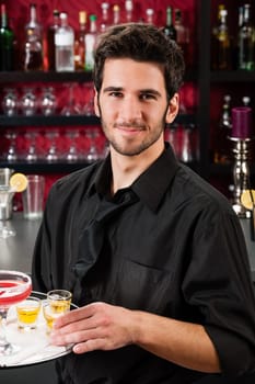 Portrait of handsome barman at bar holding tray with cocktails
