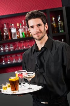 Portrait of handsome barman at bar holding tray with cocktails