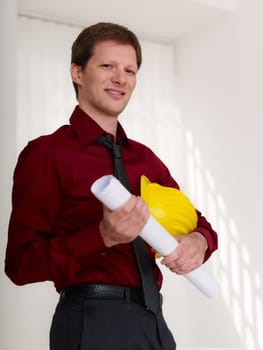 mid adult architect with helmet, holding blueprints and looking confident at camera