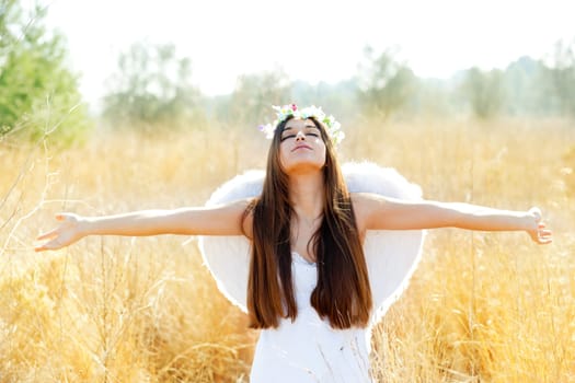 Angel etchnic woman in golden field with feather white wings and flowers crown