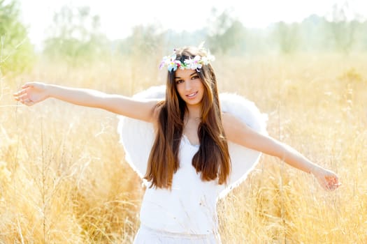 Angel etchnic woman in golden field with feather white wings and flowers crown