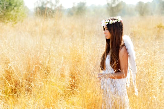 Angel etchnic woman in golden field with feather white wings and flowers crown