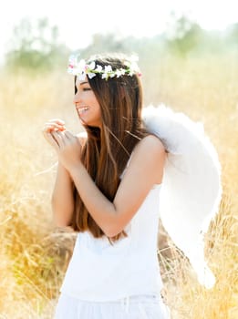 Angel etchnic woman in golden field with feather white wings and flowers crown