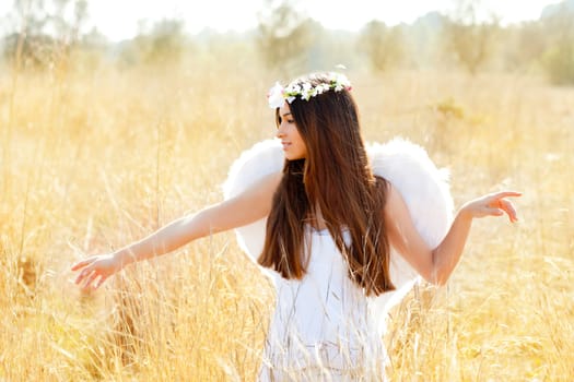 Angel etchnic woman in golden field with feather white wings and flowers crown