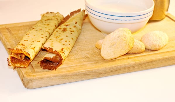 Crepes, cookies and milk on cutting board